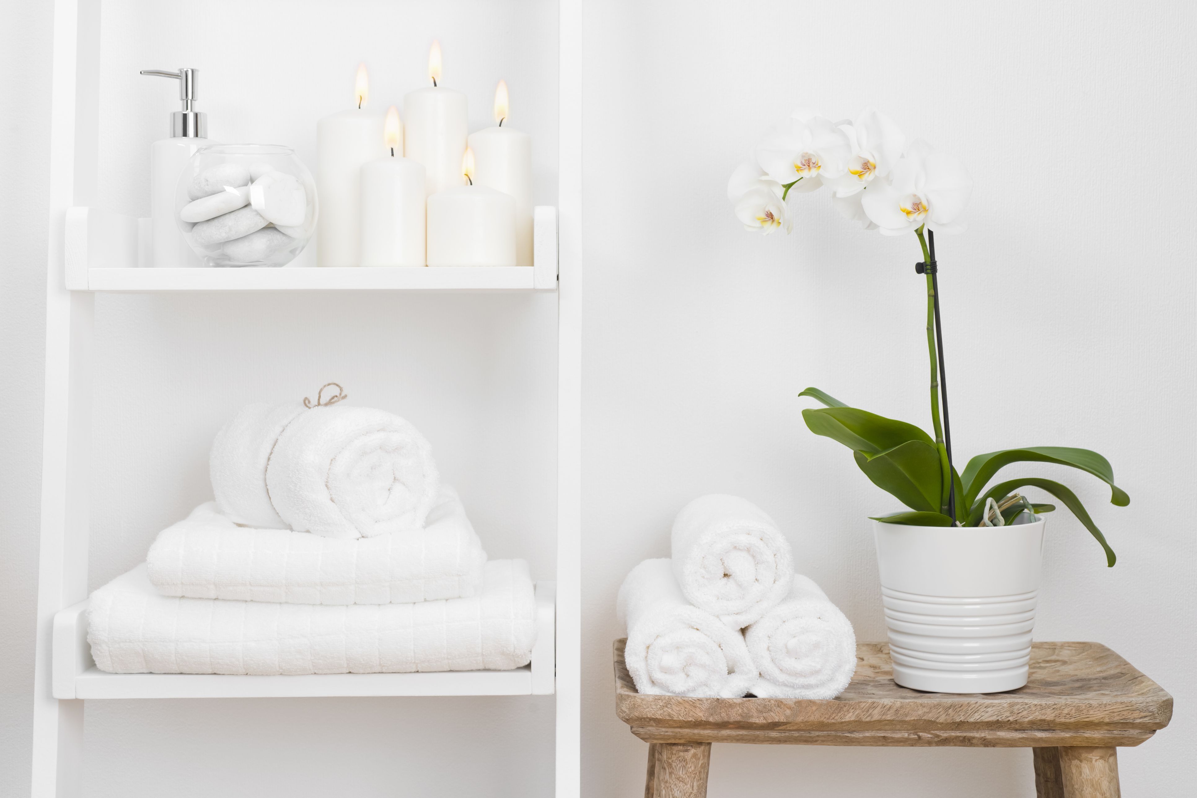 Polica s čistimi brisačami, svečami, cvetličnim lončkom na leseni mizi kopalnice