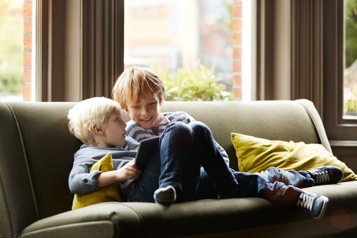 Снимка на двама малки братя, седнали на дивана в хола си с помощта на цифров таблет