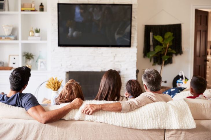 壁に取り付けられたスクリーンからテレビを見ている家族