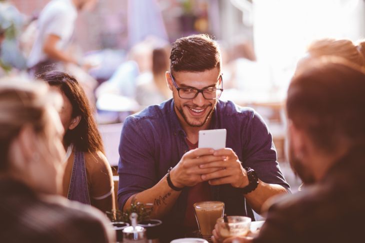 Щастлив хипстър мъж в кафене изпраща съобщения на мобилен телефон