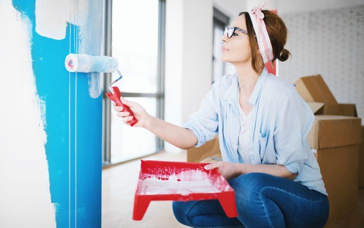 Млада жена рисува стена, наслаждавайки се на ремонта на дома си.