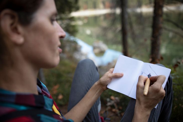 Жена турист пише дневник до планинското езеро - Стокова снимка