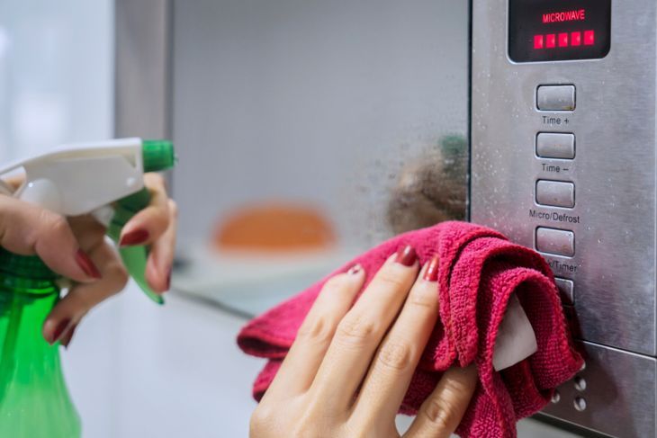 キッチンの電子レンジを掃除するためにスプレー洗剤を使用してメイドの手のクローズアップ。