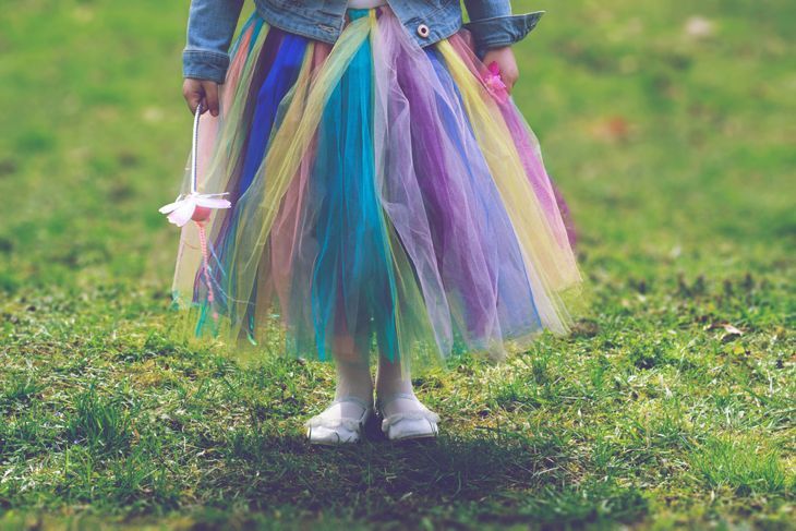 Малко момиче в цветна пола пачка, стоящо върху зелена трева, докато държи вълшебна пръчка
