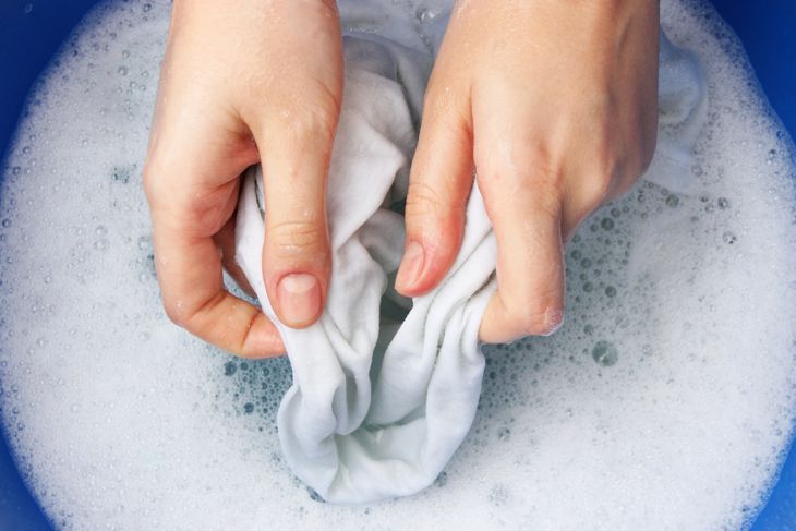 石鹸水で白いシャツを掃除する手のトリミング画像