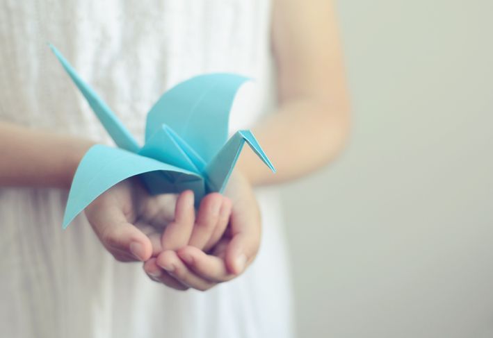 Малко момиче, което държи синя оригами птица в ръцете си