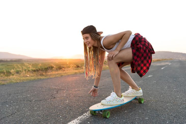 Красива млада жена кара скейтборд по селски път, по залез слънце.
