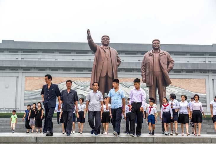 Местни жители се разхождат пред голяма статуя в Пхенян, столицата на Северна Корея в облачен ден