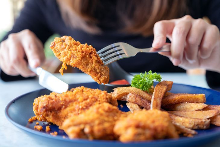 レストランでフライドチキンとフライドポテトを食べるためにナイフとフォークを使用して女性のクローズアップ画像