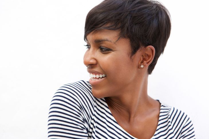 Портрет отблизо на млада афро-американка, която се усмихва и гледа настрани