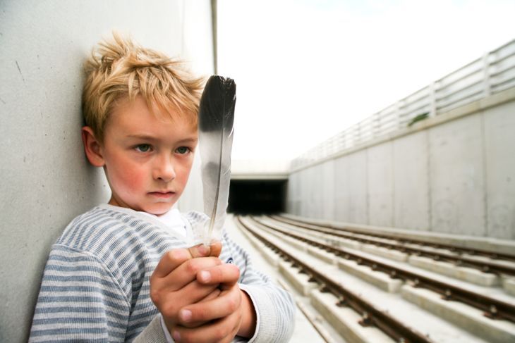 Младо момче, загледано в перо, стоящо до железопътните релси.