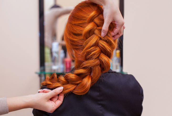 美容院で、長い髪の美しい赤毛の女の子、美容師がフレンチブレイドを編む