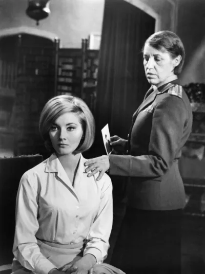 1963年の古典的なジェームズ・ボンド映画『ロシアより愛をこめて』のワンシーンで、ローザ・クレッブ役のロッテ・レーニャがタチアナ役のダニエラ・ビアンキの肩に手を置く。